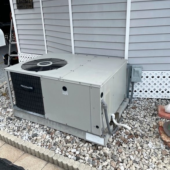 HVAC technician using a manifold gauge to check refrigerant levels on an outdoor air conditioning unit with exposed wiring and components.